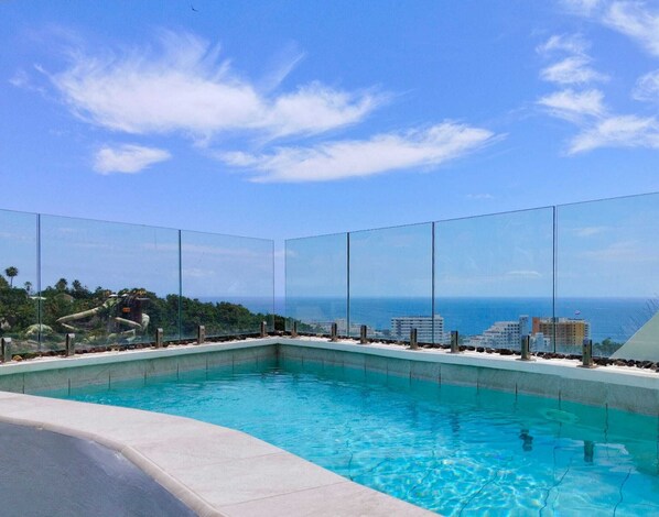 Un ciel d’un bleu éclatant, une piscine et une vue sur l’océan et les bâtiments.