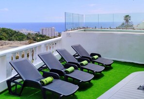 A balcony with lounge chairs and a pool, overlooking a coastal area with buildings in the distance. - Panoramic Villa Siam with a private swimming pool (Costa Adeje)