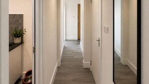 A hallway with a wooden floor, white walls, and a large mirror on the right. - 3 Bedroom House Sleeps 6 -garden -private Parking (Feltham)
