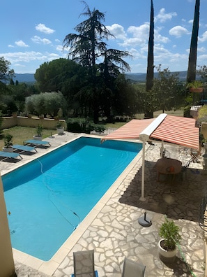 Una piscina con cubierta de piedra, rodeada de plantas en macetas y mobiliario exterior.