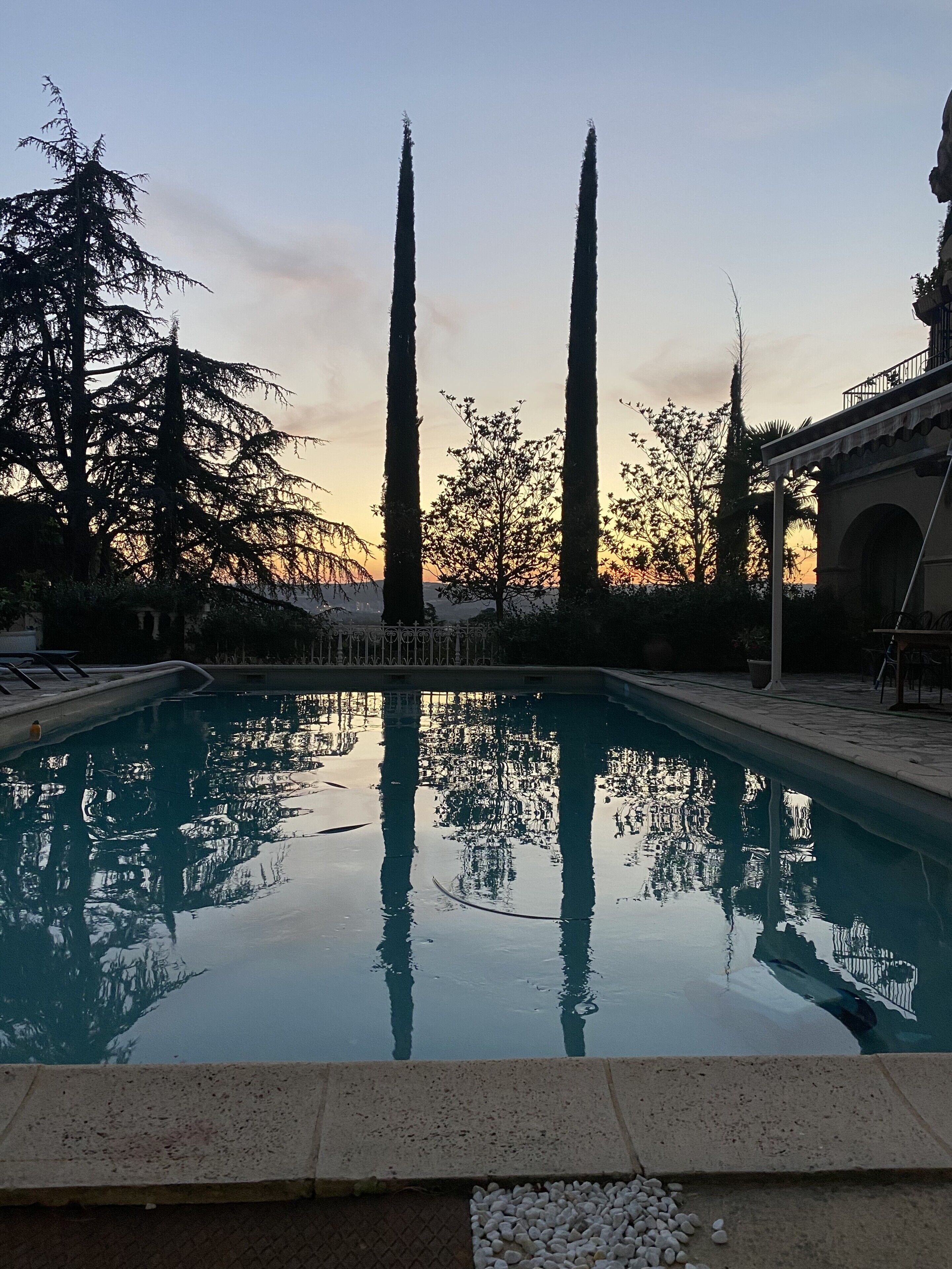 A swimming pool with a clear view of tall trees and a building in the background.