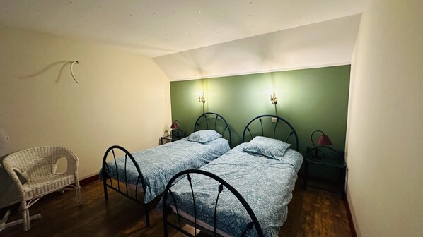 A small bedroom with two single beds, a chair, and a nightstand with a lamp.