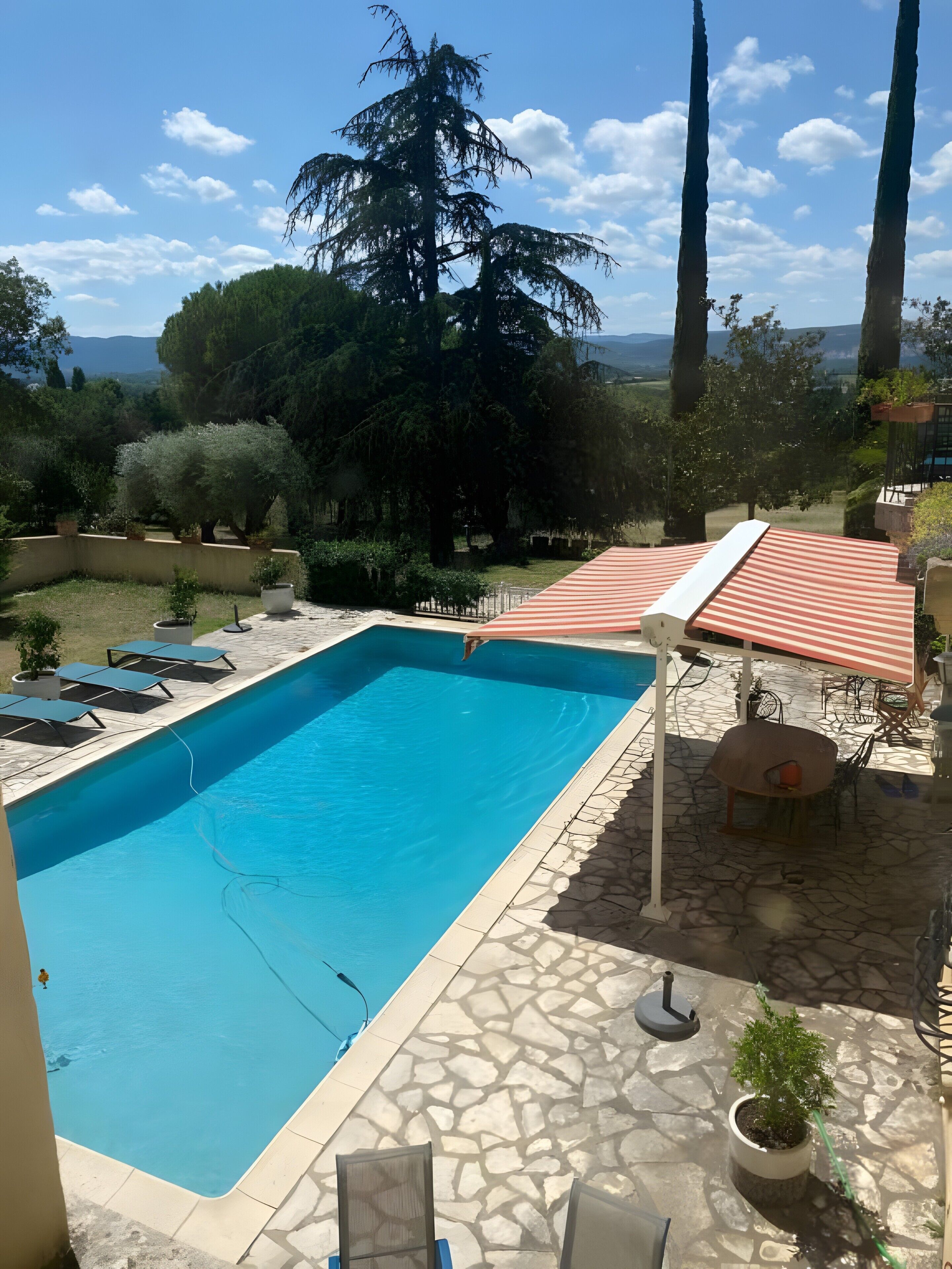 Une piscine rectangulaire bordée d’une terrasse en pierre, entourée de chaises longues et d’un espace salon abrité.