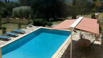 Une piscine rectangulaire bordée d’une terrasse en pierre, entourée de chaises longues et d’un espace salon abrité.