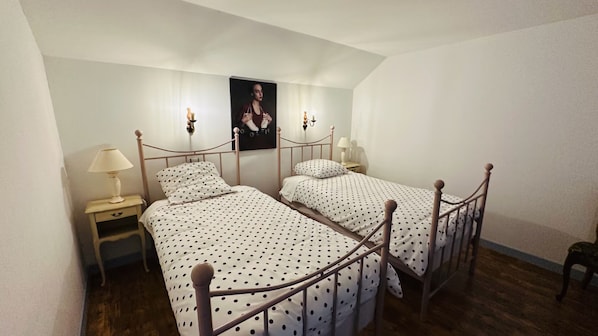 A bedroom with two single beds, a nightstand with a lamp, and a poster on the wall.
