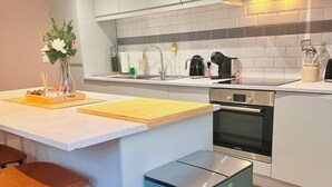 Une cuisine moderne dotée d’un îlot central, de tabourets de bar, d’un four Bosch et d’une petite poubelle.