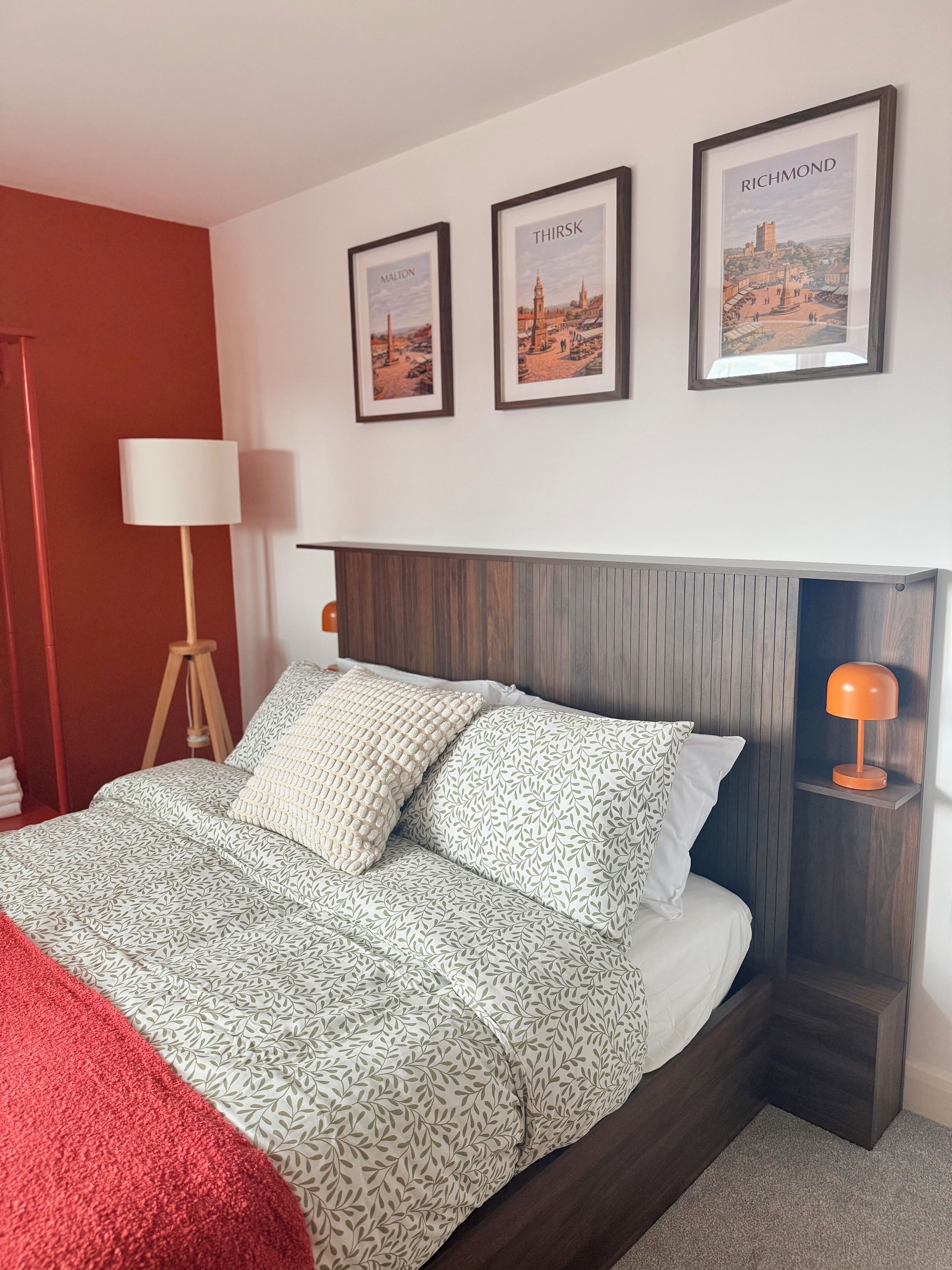 A neatly made bed with patterned bedding, a bedside lamp, and framed pictures on the wall.