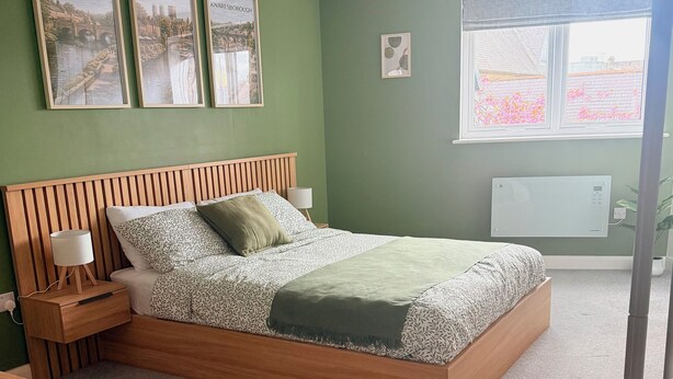 Un dormitorio con cama de madera, paredes verdes y cuadros enmarcados de ciudades.
