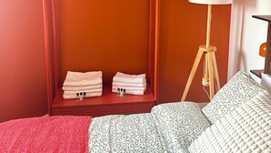 Una habitación con una cama, un armario rojo, una planta colgante y una lámpara de pie.