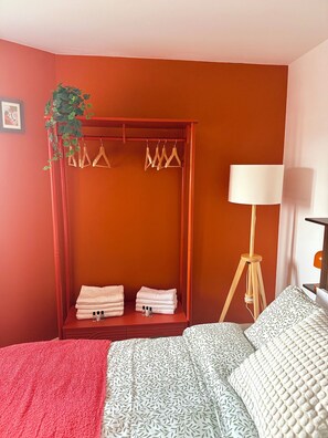 Ein Zimmer mit einem Bett, einem roten Kleiderschrank, einer hängenden Pflanze und einer Stehlampe.