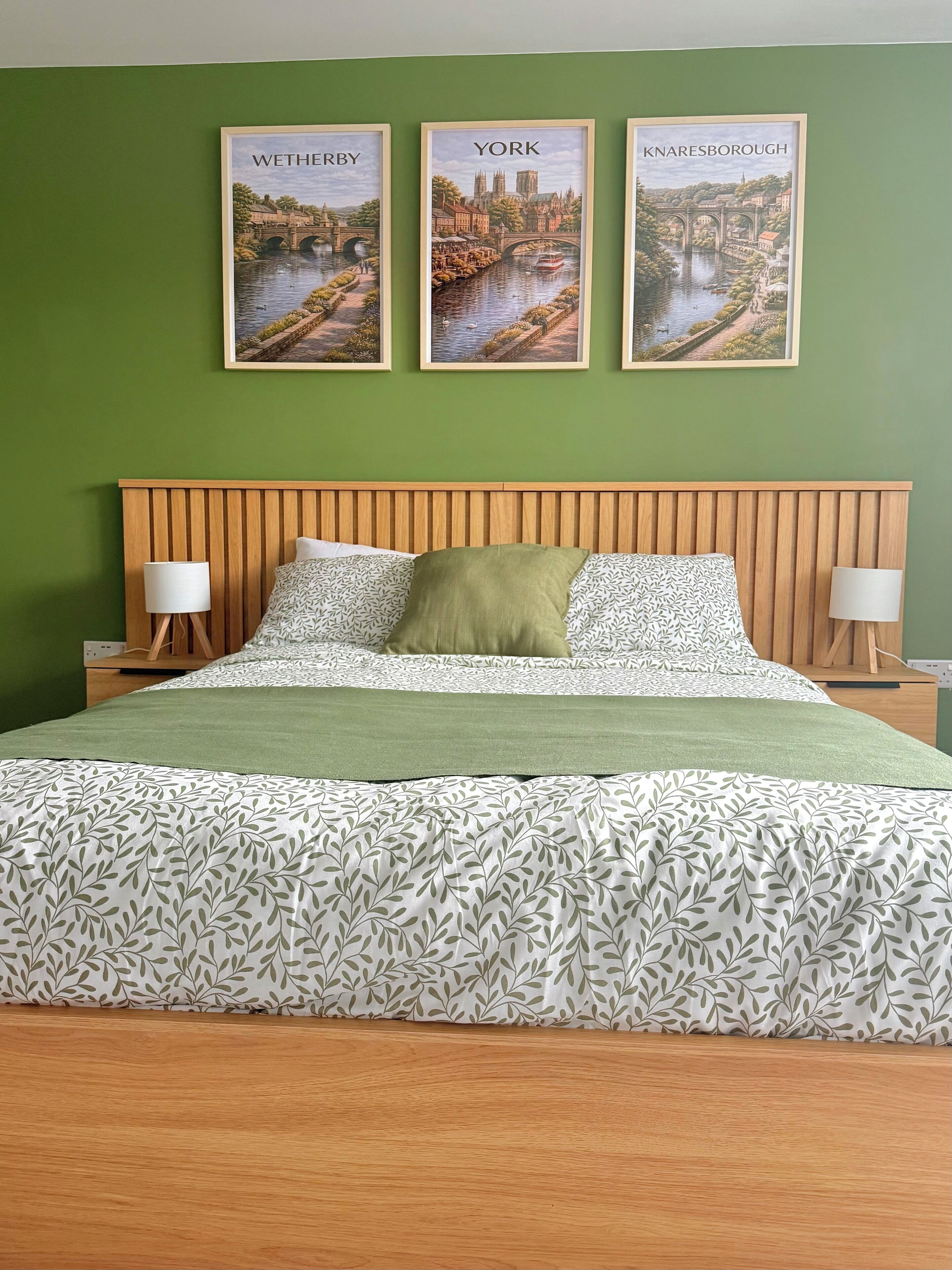A bed with a patterned bedspread, a wooden headboard, and three framed pictures of cities on the wall.