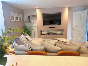Ein Wohnzimmer mit einer Couch, einem flachbildfernseher an der Wand, einer Tür und einer Pflanze.