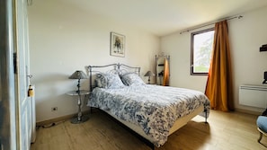 Un dormitorio con cama, mesitas de noche, una ventana con cortinas y un aire acondicionado de pared.