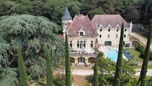 Un edificio grande con piscina, rodeado de árboles y un jardín.