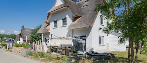 A white house with a thatched roof, a paved driveway, and a garden with various plants.