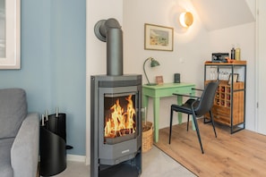 A modern living room with a wood-burning stove, a green desk, a chair, and a wine rack. - LYKKE LUNA Vacation Home with Sauna and Fireplace on Usedom (Zirchow)
