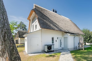 A white building with a thatched roof, a front door, and a small air conditioning unit. - LYKKE LUNA Vacation Home with Sauna and Fireplace on Usedom (Zirchow)
