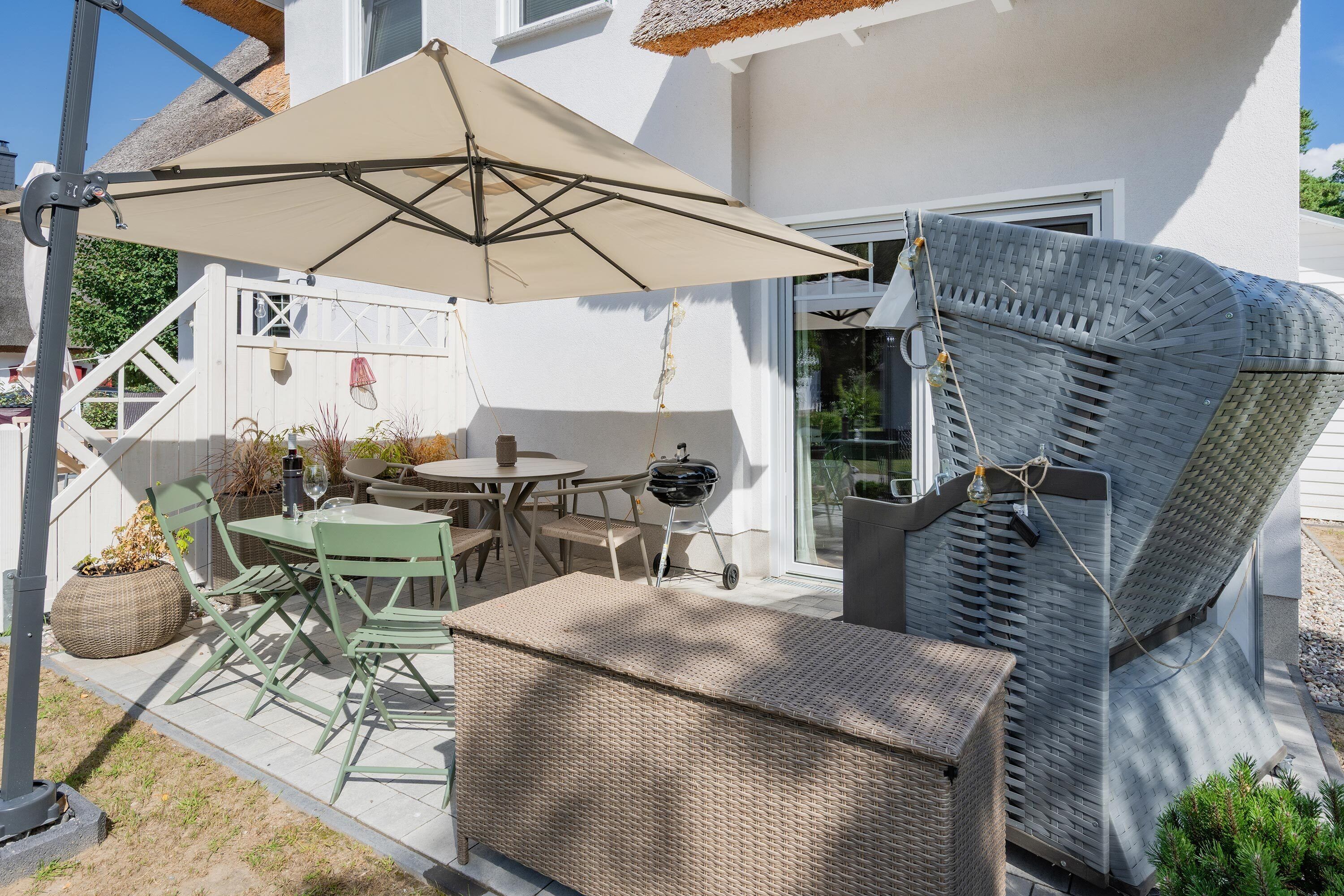 An outdoor patio with a table and chairs, a grill, and a large umbrella.