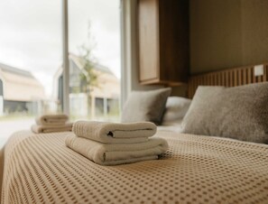 Ein ordentlich bezogenes Bett mit einer strukturierten Tagesdecke und einem Stapel gefalteter Handtücher.