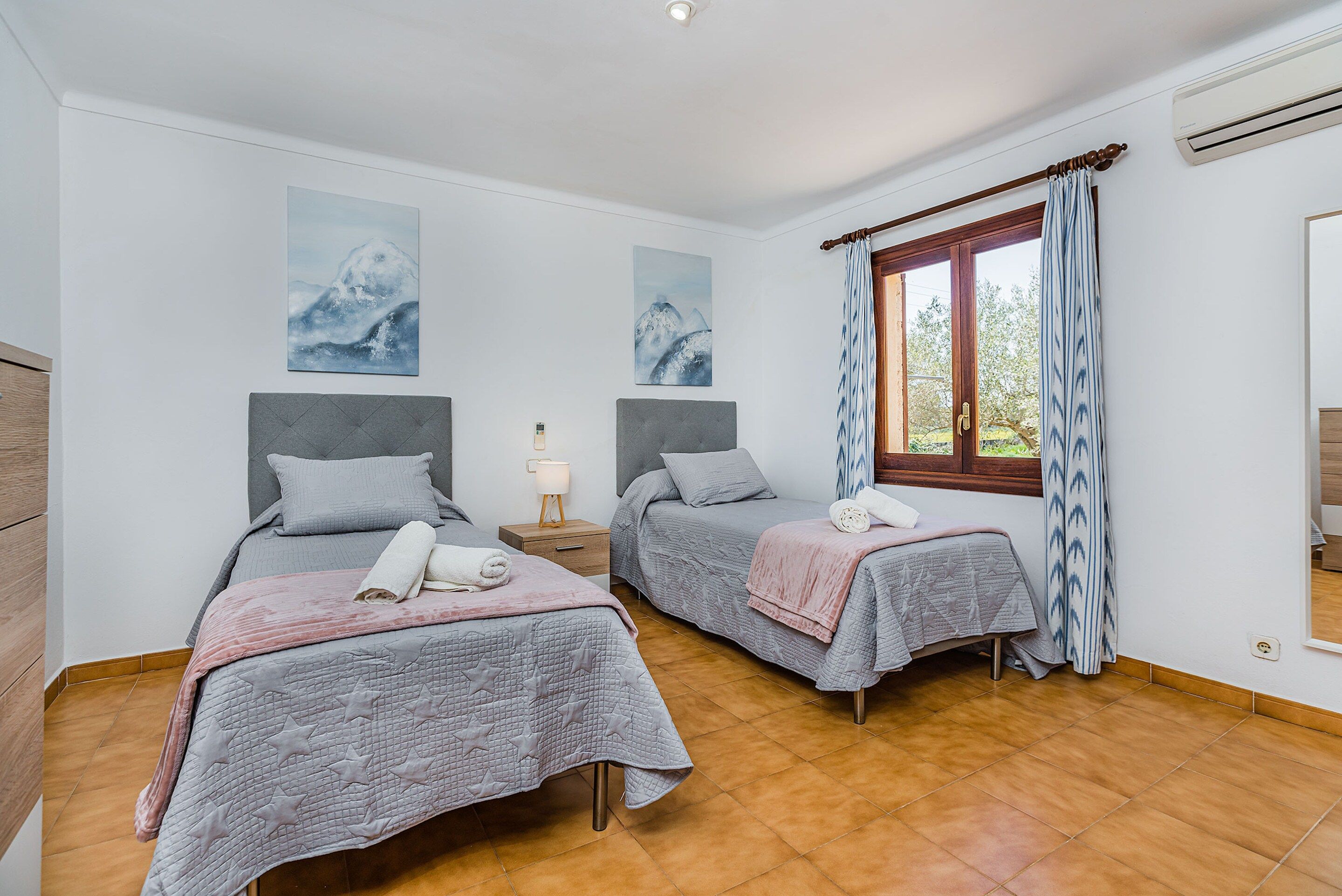 A bedroom with two beds, a window with curtains, and artwork on the wall.