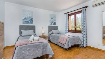 A bedroom with two beds, a window with curtains, and artwork on the wall.