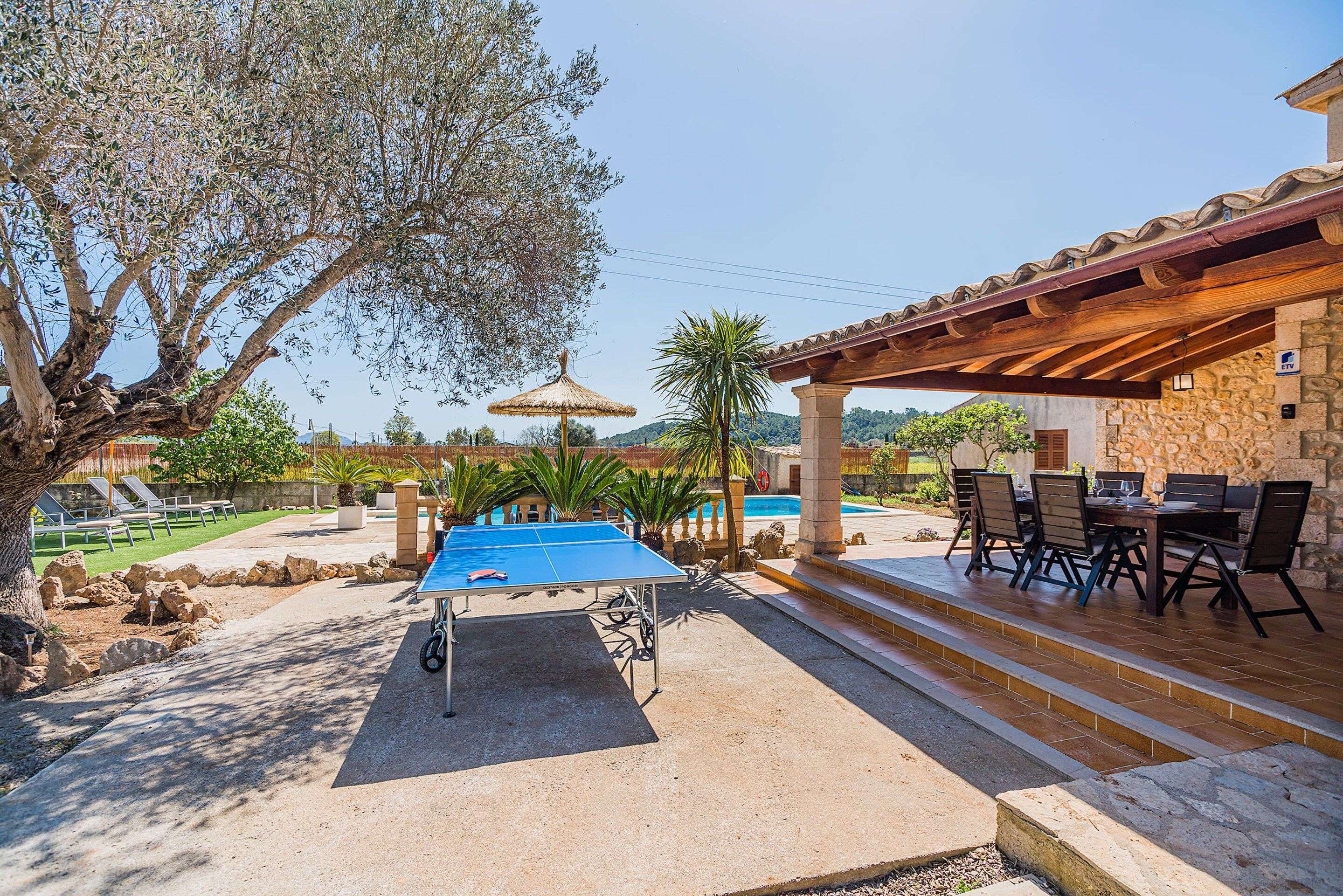 An outdoor pool area with a ping pong table, lounge chairs, and a covered seating area with a stone wall.