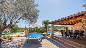 Ett utomhusområde med en pool, ett bord för bordtennis, solstolar och en överbyggd sittplats med en vägg av sten.