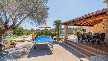 An outdoor pool area with a ping pong table, lounge chairs, and a covered seating area with a stone wall.