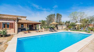 A swimming pool with lounge chairs, a patio area, and a stone building with a tiled roof.