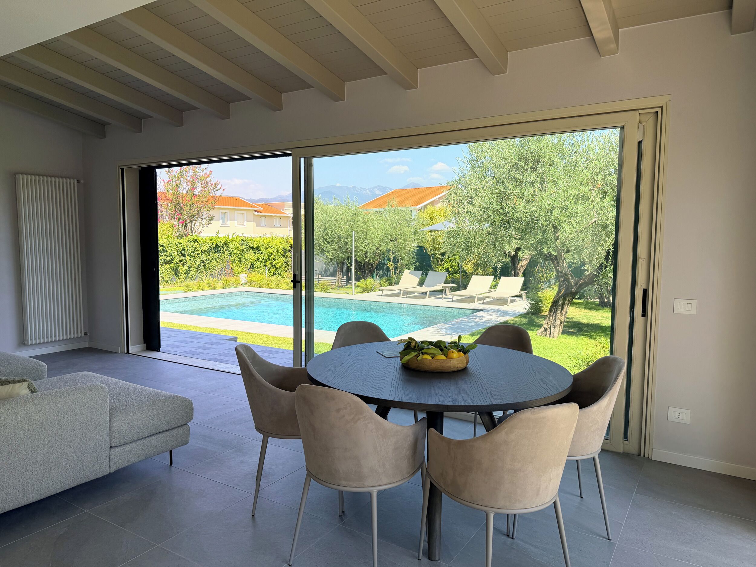 A modern living room with a pool view, a dining table with chairs, and a sofa.