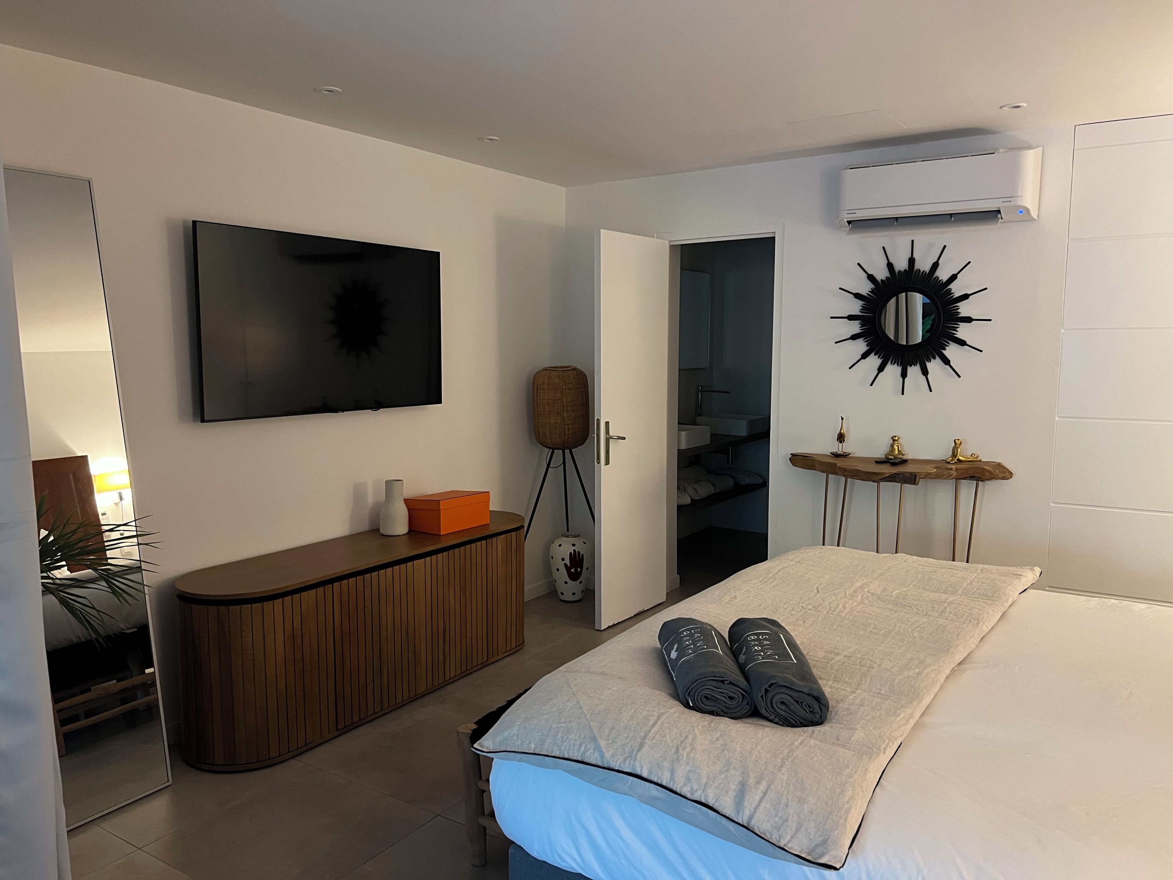 Une chambre moderne avec un lit, une télévision, une armoire et une salle de bain visible à travers une porte ouverte.