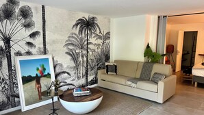 Ein Wohnzimmer mit einer Couch, einem Couchtisch, einem gerahmten Bild und einer großen Pflanze.