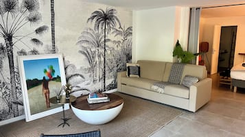 Un salon avec un canapé, une table basse, un tableau encadré et une grande plante.