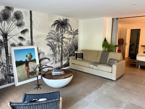 A living room with a sofa, a coffee table, a framed picture, and a large plant. - The Coconut | Cozy 1-Bedroom Apartment in the Hills of Saint Jean (Saint Jean)