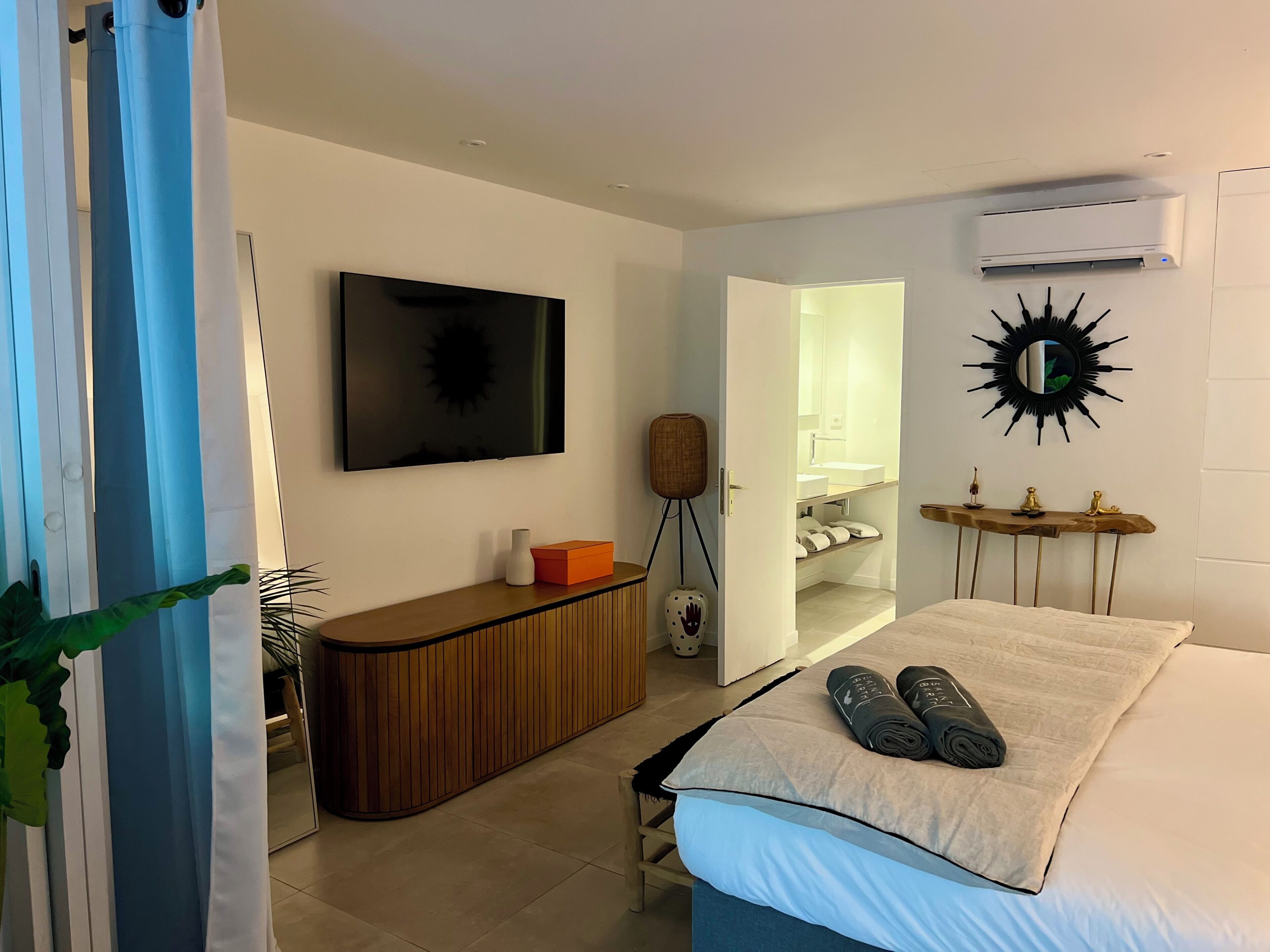 Une chambre d’hôtel avec un lit, une télévision, une console en bois, un miroir et une porte ouverte donnant sur une salle de bain.