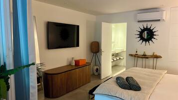 Une chambre d’hôtel avec un lit, une télévision, une console en bois, un miroir et une porte ouverte donnant sur une salle de bain.