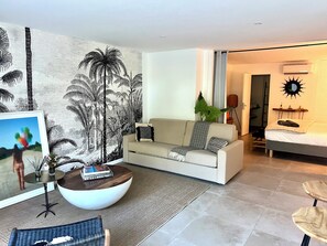 A modern living room with a sofa, a coffee table, and a large wall mural. - The Coconut | Cozy 1-Bedroom Apartment in the Hills of Saint Jean (Saint Jean)