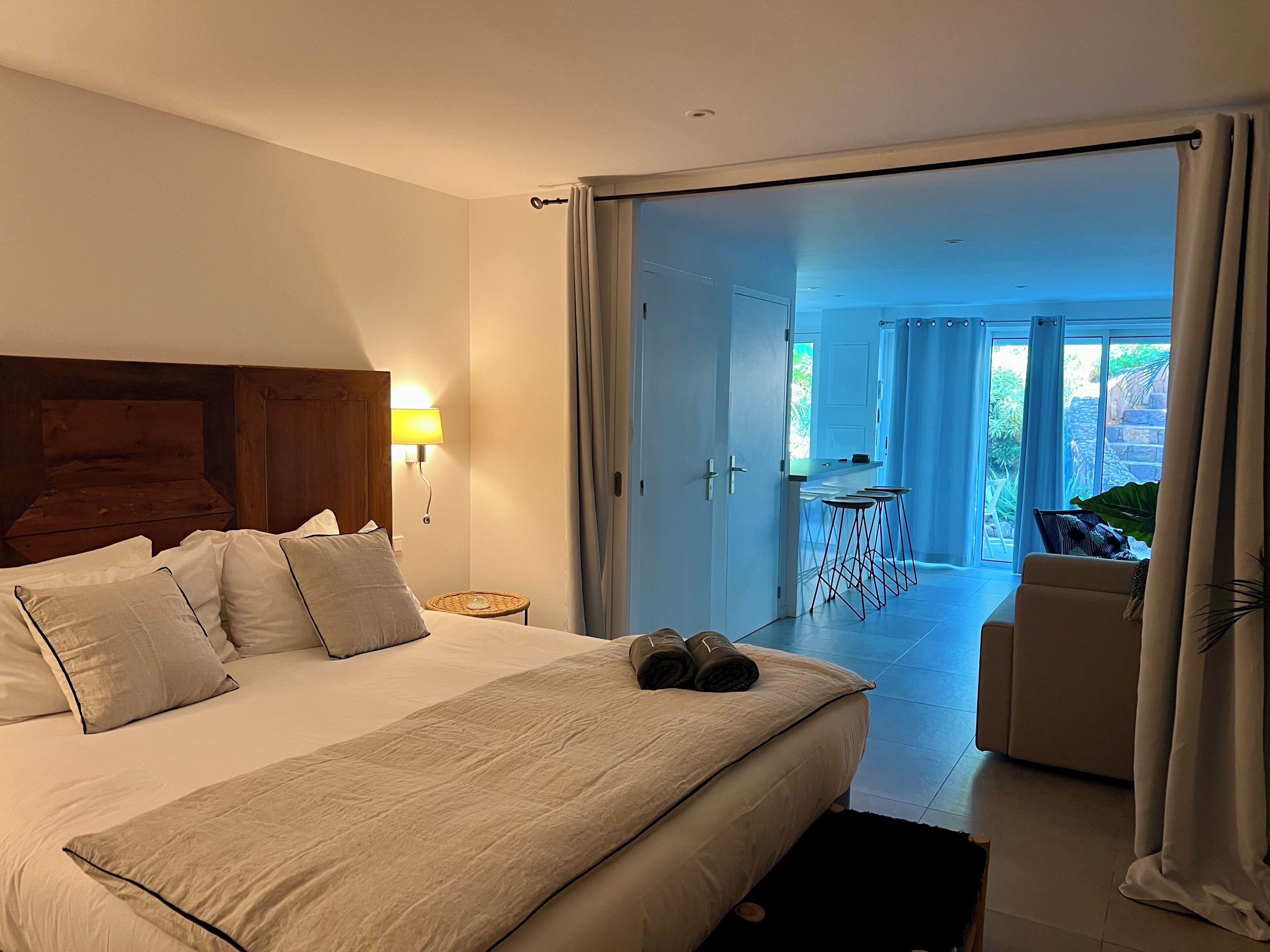 Een hotelkamer met een bed, een nachtkastje, een lamp, uitzicht op het buitengebied en een zithoek.