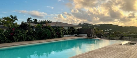 Una piscina con cubierta de madera, rodeada de abundante vegetación y vistas a un paisaje montañoso.