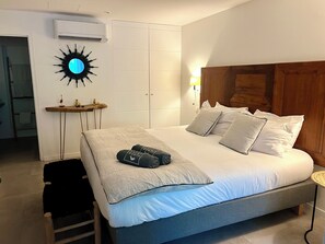 A bedroom with a bed, bedside table, wall-mounted air conditioning unit, and a unique wall decoration. - The Coconut | Cozy 1-Bedroom Apartment in the Hills of Saint Jean (Saint Jean)