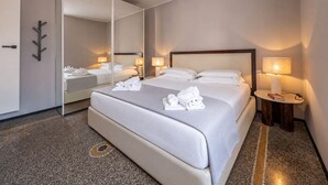 A hotel room with a large bed, a bedside table with a lamp, a mirror, and a wardrobe. - LUX APARTMENT - Comfort and Style in the Heart of Santa Margherita (Santa Margherita Ligure)