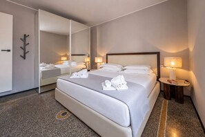 Een hotelkamer met een groot bed, een nachtkastje met een lamp, een spiegel en een garderobe.