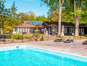 Ein Schwimmbecken mit einem umzäunten Bereich, ein Gebäude mit Solaranlagen und Bäume im Hintergrund.