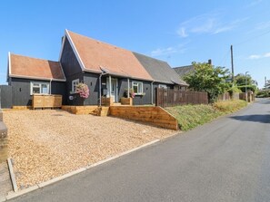 Ein zweigeschossiges Haus mit einem geneigten Dach, einer Schotterauffahrt und einem Holzzaun.