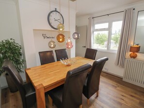 Ein Essbereich mit einem Holztisch, sechs Stühlen, einer Wanduhr, dekorativen Hängeleuchten und einem Blumentopf.