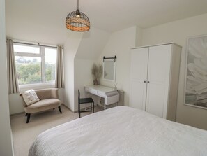 Ein Schlafzimmer mit einem Bett, einem Schreibtisch, einem Stuhl, einem Kleiderschrank und einem Fenster mit Vorhängen.