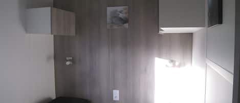 Habitación pequeña con dos camas, una mesita y un estante en la pared.