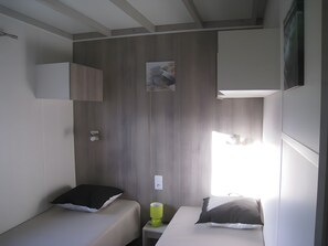 A compact room with two beds, a small table, and a wall-mounted shelf.