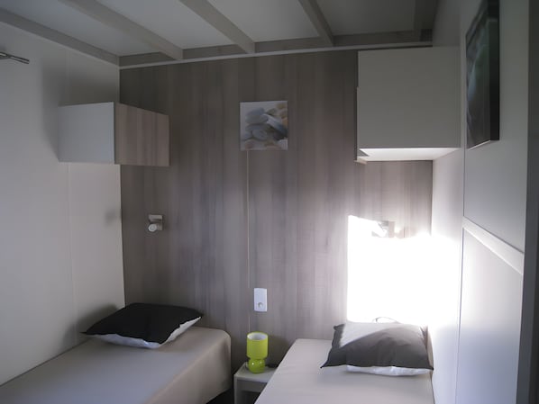 A compact room with two beds, a small table, and a wall-mounted shelf.