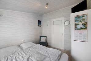 A bedroom with a bed, a chair, a door, and a wall with a calendar and a framed picture.